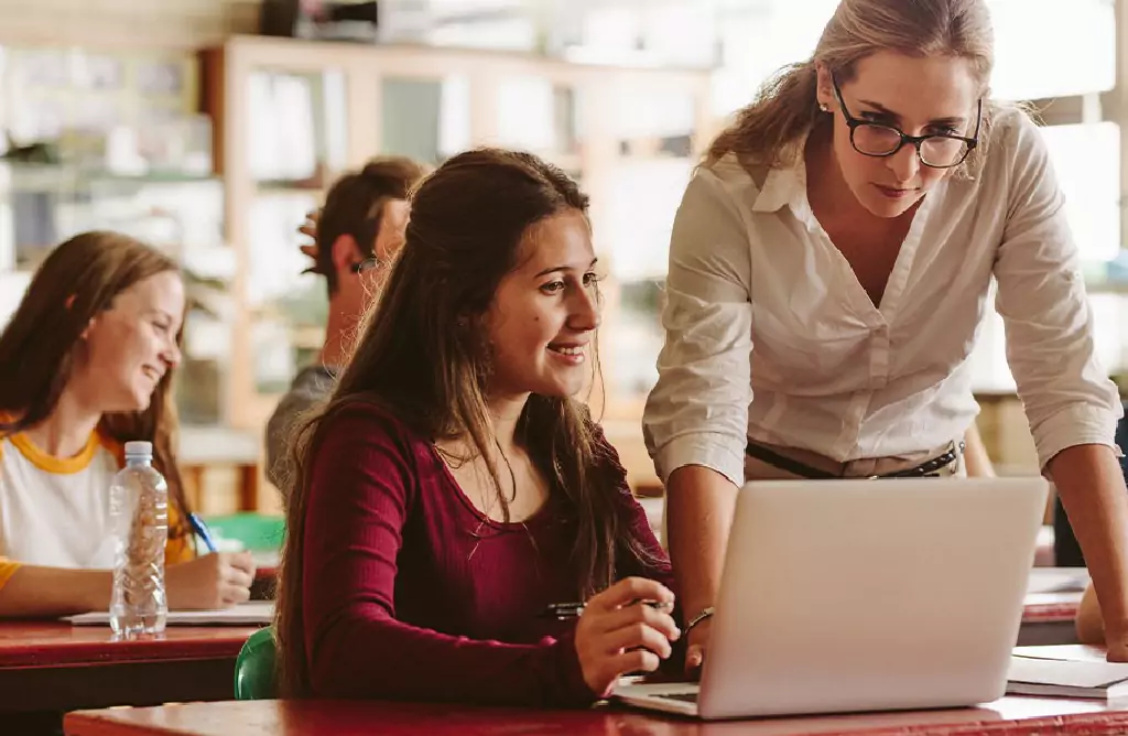 Teacher Assisting a Student with a Laptop in Class
