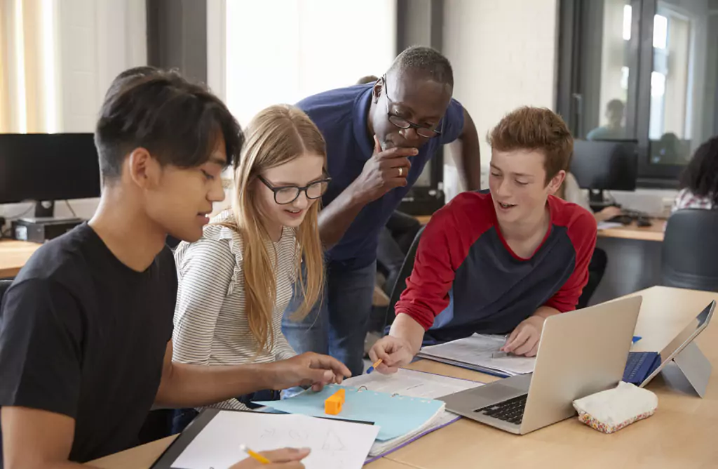  A teacher is Helping Three Students with their Work on a Laptop in a Classroom