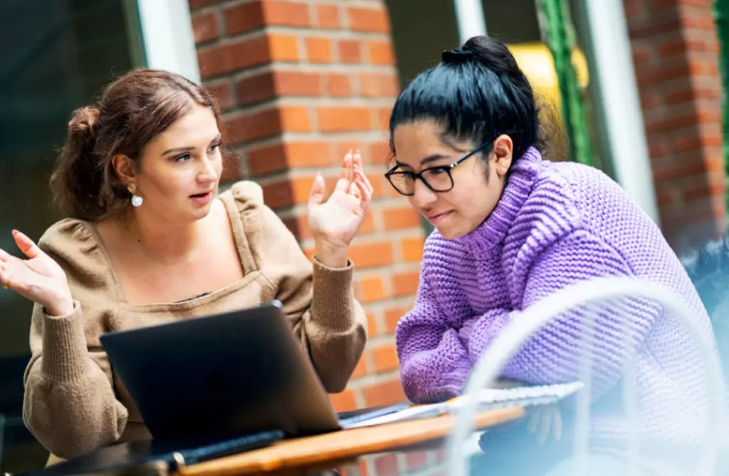 Two Students Discussing Coursework at a Laptop on Campus