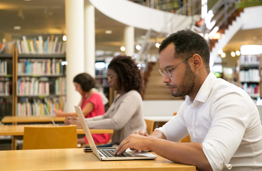 International Student Using a Laptop in a University Library Study Space